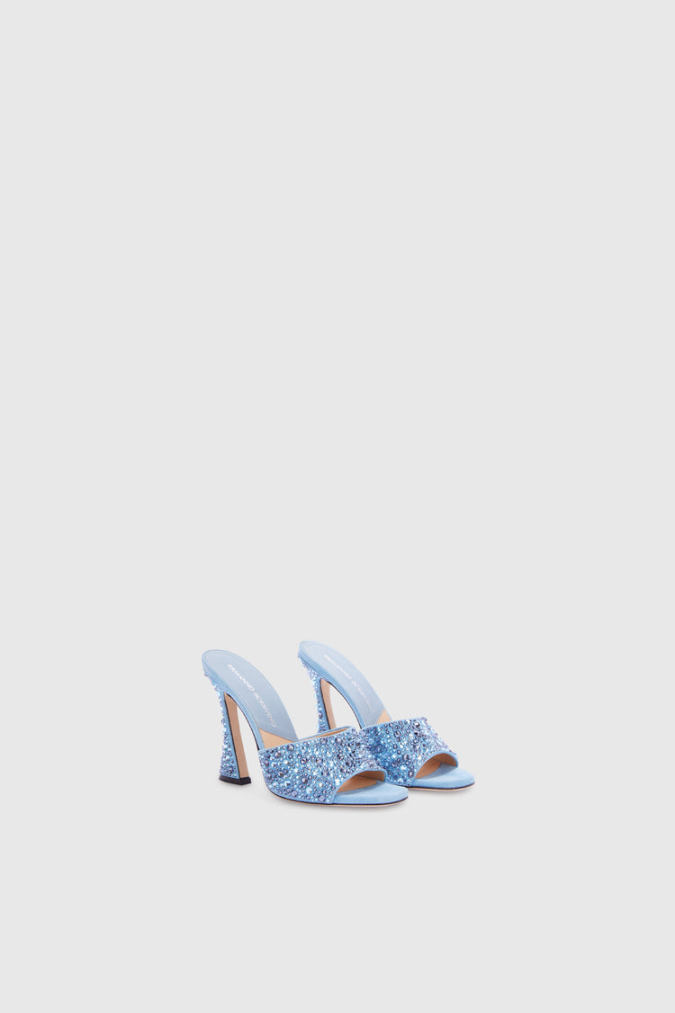Elegante paio di scarpe modello mule con tacco alto azzurro con dettagli in cristallo, mostrate su sfondo chiaro che ne esalta il design lussuoso