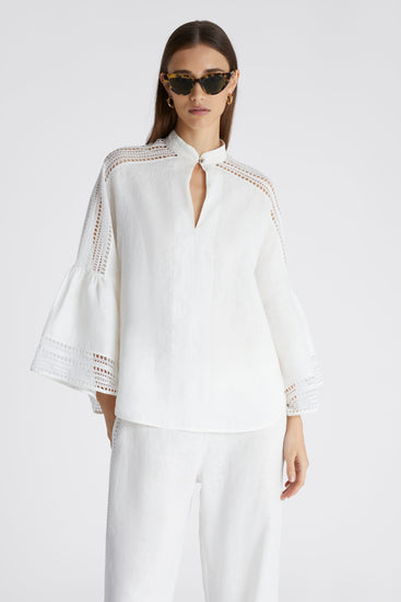 Model in white pure linen blouse with cap sleeves and small round button on the collar