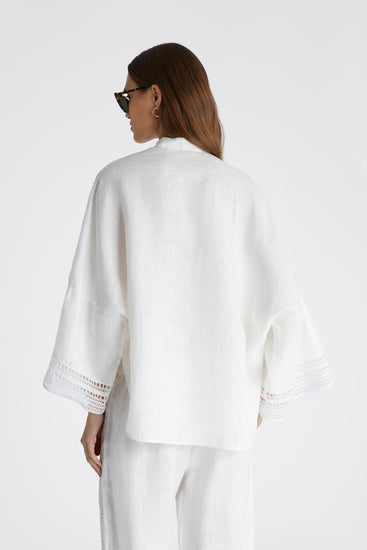 Rear view of model in white pure linen blouse with cap sleeves and small round button on the collar