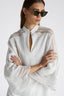 Close-up of model in white pure linen blouse with cap sleeves and small round button on the collar