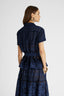 Rear view of model in navy broaderie anglaise short sleeve cotton shirt with a sash at waistline