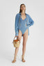Model showcasing Denim Trikini One-piece with sretch gold piping and strings on the back with denim shirt over